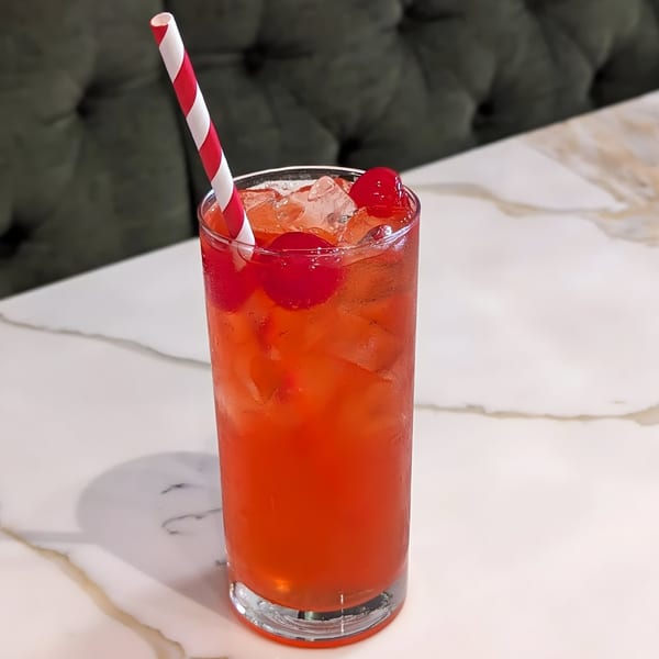 A vibrant red drink with ice and cherries, served in a tall glass with a striped straw.