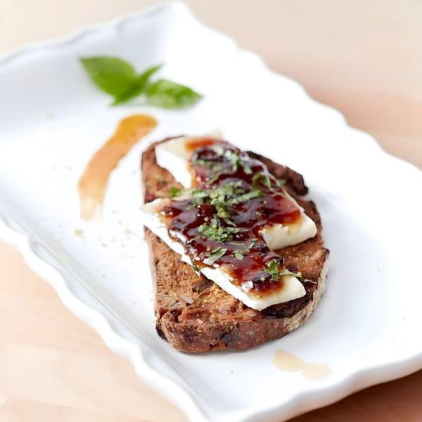 Toasted bread with brie cheese, fig jam, and fresh basil on a white rectangular plate.
