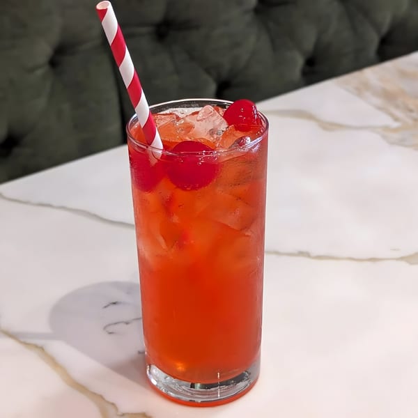 A vibrant red drink with ice and cherries, served in a tall glass with a striped straw.