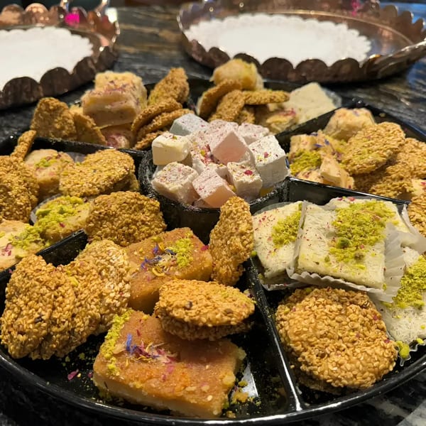 A black platter filled with various Middle Eastern sweets, including sesame cookies, halva, and Turkish delight.