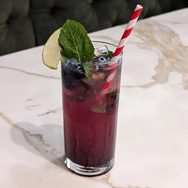 A refreshing blueberry drink with mint, lime, and a red-striped straw on a marble table.
