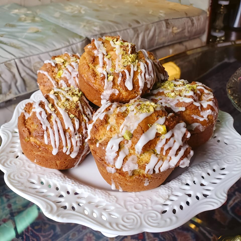 Pistachio Cafe muffins with white icing and green pistachio crumbles on a decorative white plate.