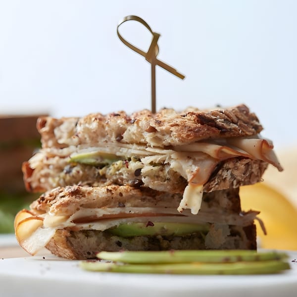 A Pistachio Cafe turkey and avocado sandwich on whole grain bread, skewered with a decorative pick.
