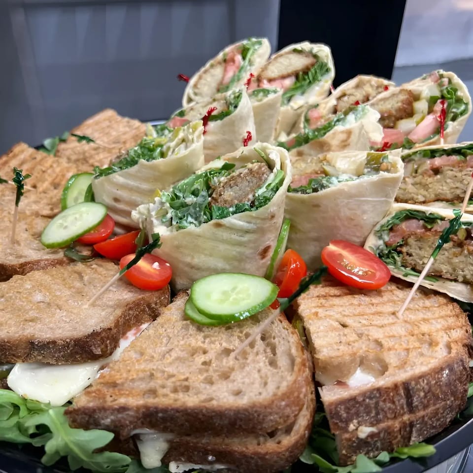 A platter of grilled sandwiches and falafel wraps garnished with cherry tomatoes and cucumber slices.