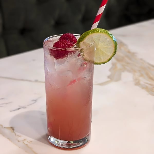 Pink raspberry drink with ice, a lime slice, and a red and white striped straw on a marble table.