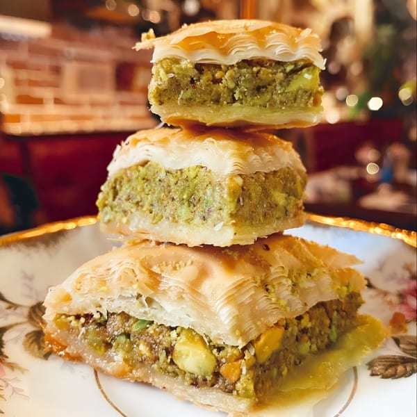 Three pieces of Pistachio Cafe baklava stacked on a decorative white and gold plate.