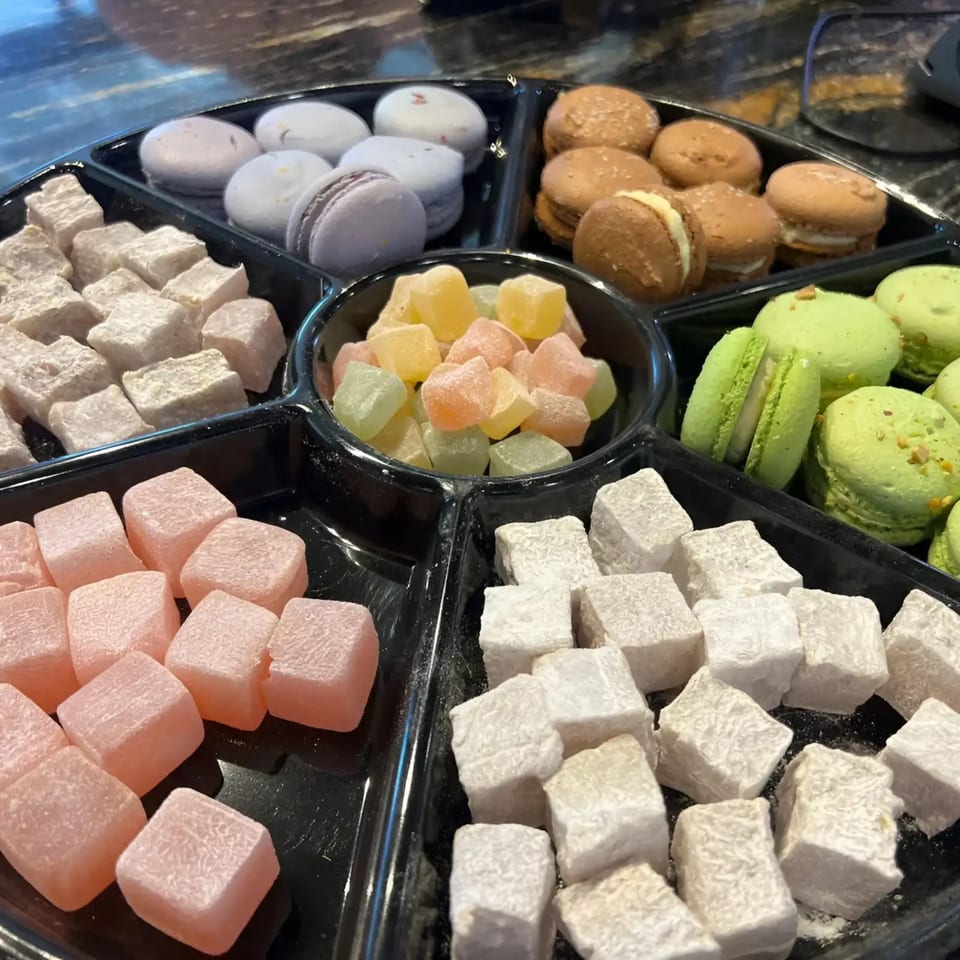 A black segmented tray filled with various colorful macarons and Turkish delights.
