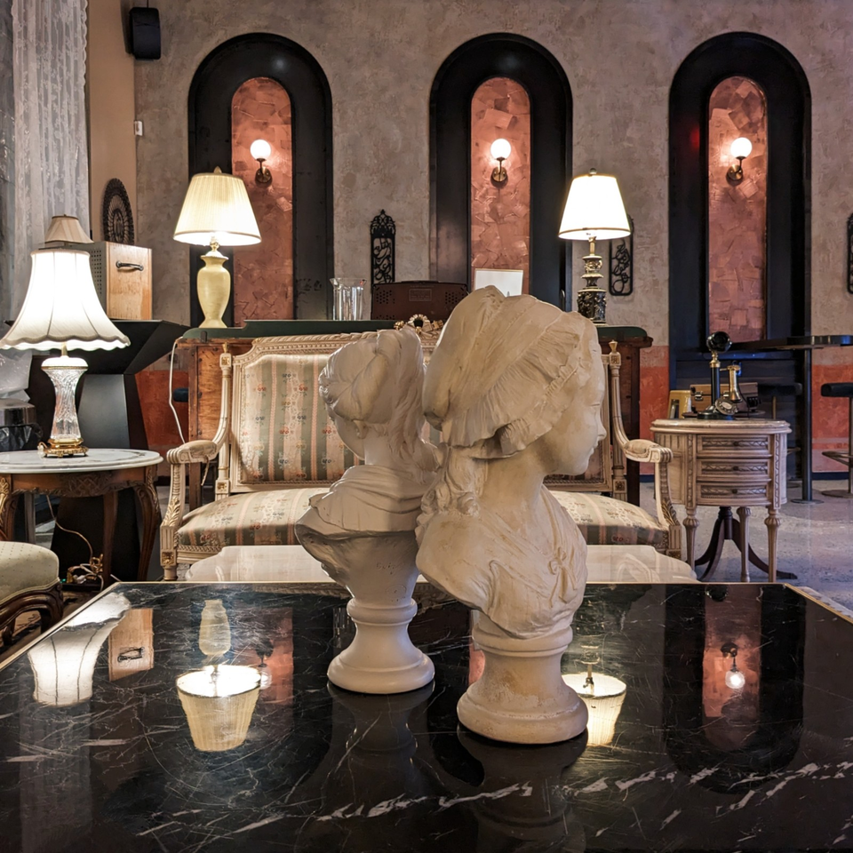 Elegant restaurant lounge with classical busts on a black marble table, antique sofa, lamps, and arched illuminated wall niches.