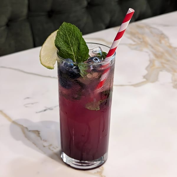 A refreshing blueberry drink with mint, lime, and a red-striped straw on a marble table.