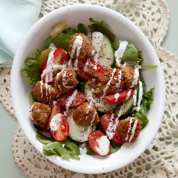 Falafel salad with lettuce, tomatoes, cucumbers, and a creamy white dressing in a white bowl.