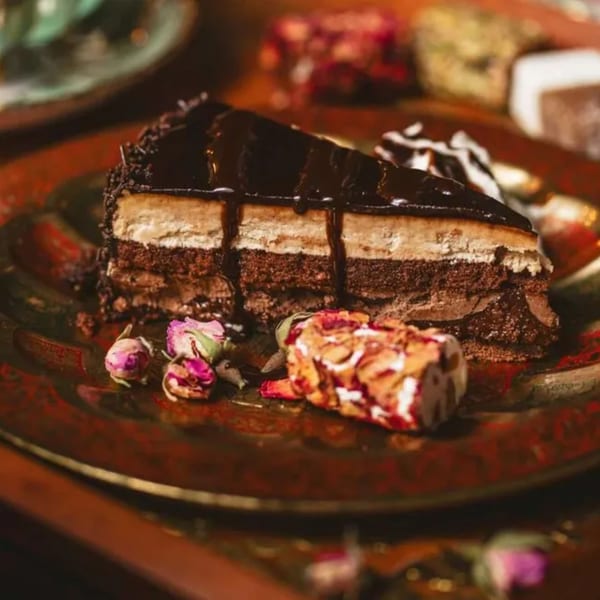 A slice of chocolate cake with creamy layers and chocolate drizzle, garnished with dried rosebuds.