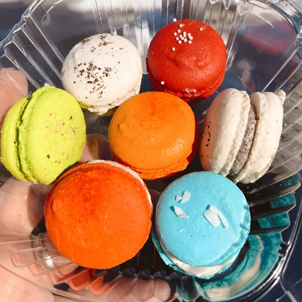 Seven colorful macarons in a clear plastic container, including red, orange, green, blue, and white.