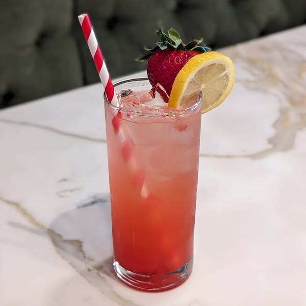 A refreshing strawberry lemonade with ice, a lemon slice, and a red and white straw.