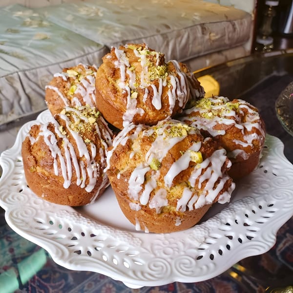Pistachio Cafe muffins with white icing and crushed pistachios on a decorative white plate.