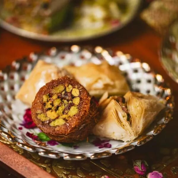 A decorative plate holds a variety of baklava pastries, including one with a pistachio filling.