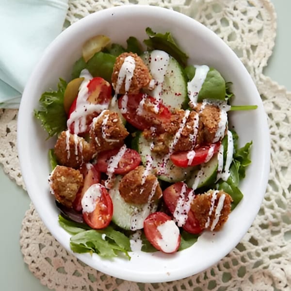 Falafel salad with fresh greens, sliced cucumbers, cherry tomatoes, and creamy white dressing.