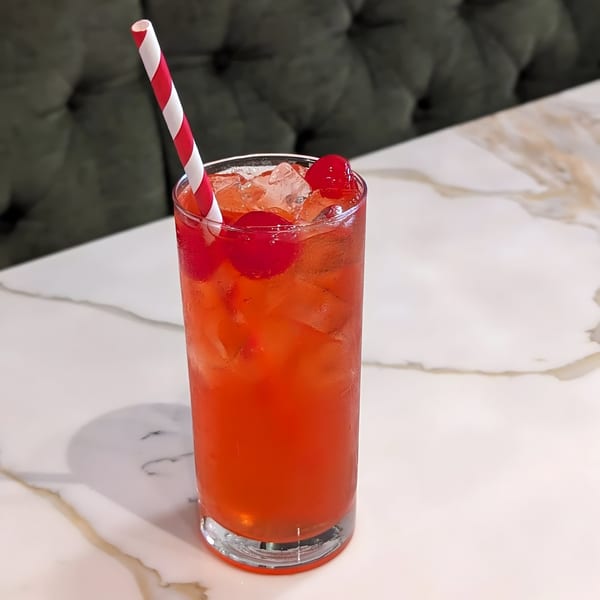 A red drink with ice and cherries, garnished with a red and white striped straw.